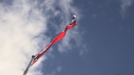 Waving-the-Kingdom-of-Thailand-flag-on-a-pole-with-blue-sky-and-white-clouds-in-the-background