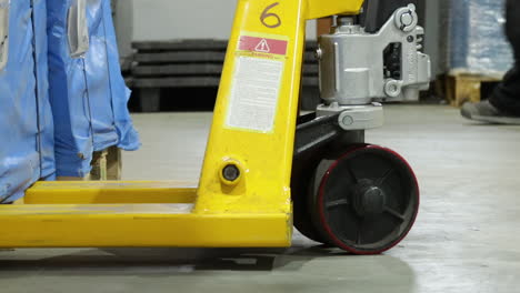 worker pulls and drags pallet truck out from wooden crates in factory, zoom out low angle static