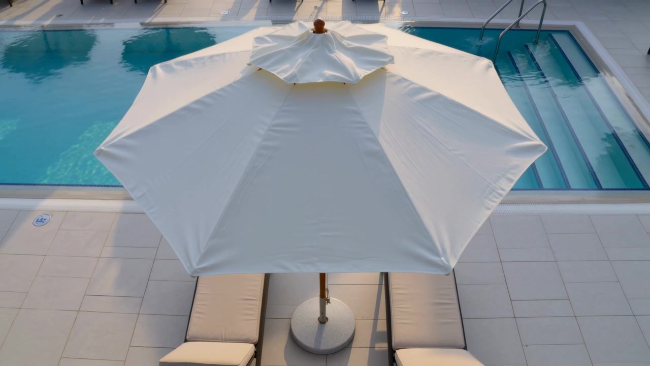 Telecamera che si allontana rivelando un ombrellone bianco sopra il patio della piscina, due sedie imbottite e il corrimano delle scale.