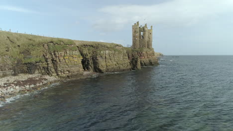 aerial rising shot moving along the coastline towards keiss castle on a sunny day, caithness, scotland