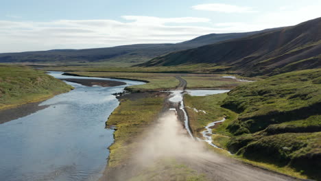 Drone-view-vehicle-speeding-on-dust-road-in-Iceland-exploring-amazing-landscape.-Aerial-view-off-road-4x4-car-driving-along-gravel-trail-path-in-mossy-icelandic-highlands.-Commercial-insurance