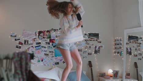 happy teenage girl dancing on bed at home to music enjoying celebrating weekend having fun singing wearing pajamas in bedroom