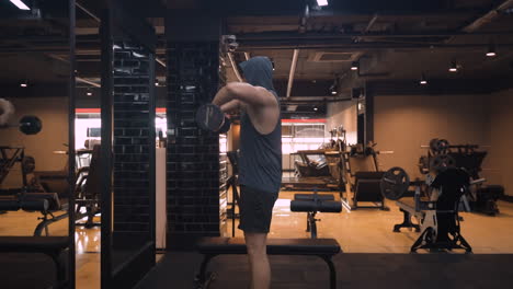 sporty man trains shoulders, performing barbell raise exercise in empty gym in front of mirror - side view