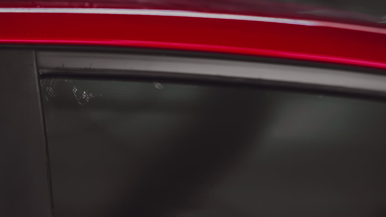 ingeniero de cerca con guantes negros y usando un paño de microfibra verde para limpiar el espejo de la ventana lateral del coche rojo