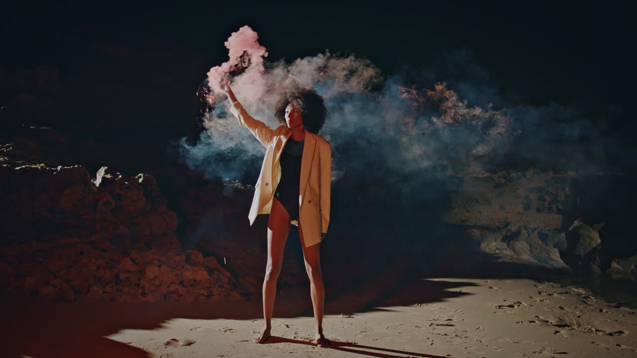Party girl holding smoke grenade at night beach. Creative woman waving bomb