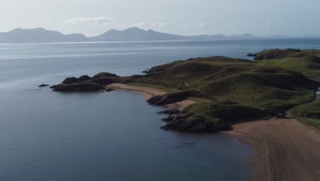 Vista-Aérea-Decente-A-La-Playa-De-La-Isla-Ynys-Llanddwyn-Con-La-Brumosa-Cordillera-De-Snowdonia-A-Través-Del-Mar-Irlandés-Al-Amanecer.