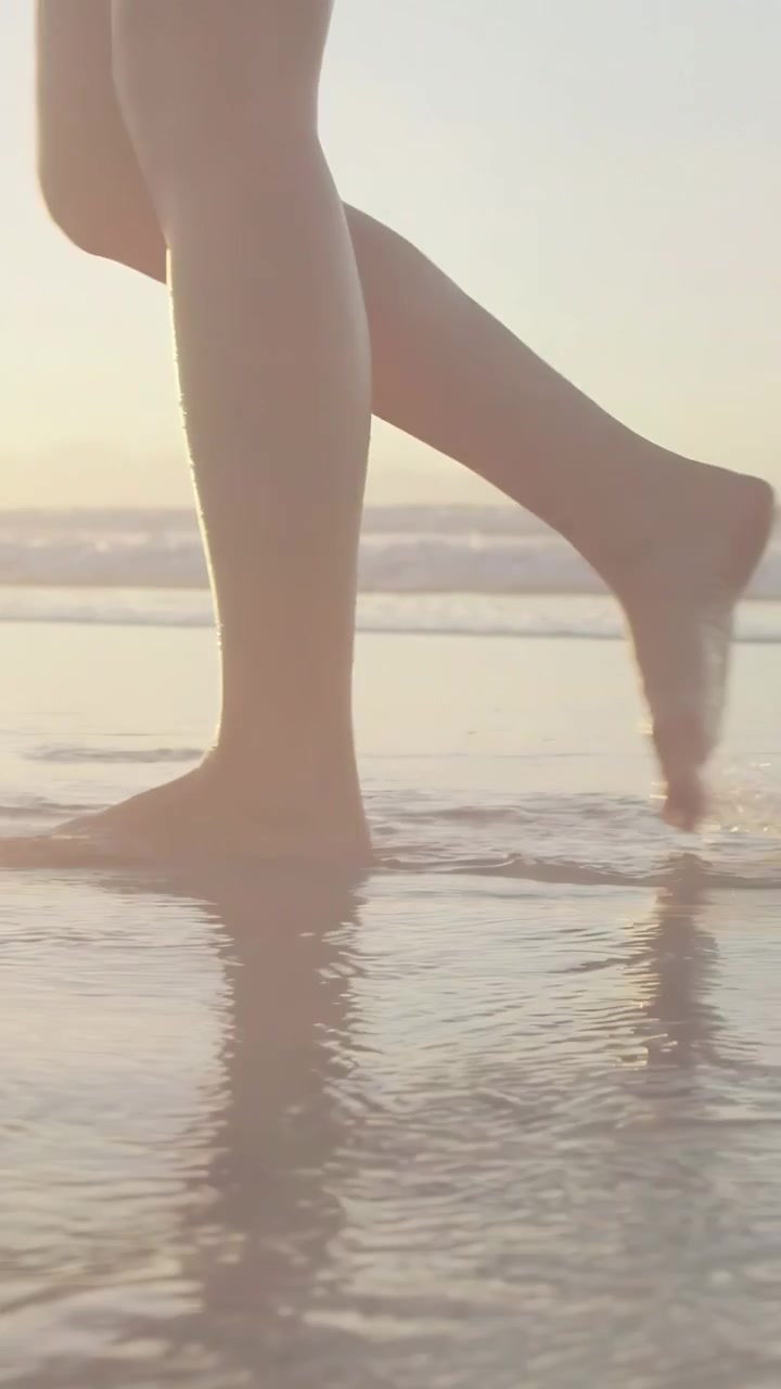Video verticale: Donna cammina sulla riva, il piede nell'acqua crea increspature, un bagliore animato aiuta il movimento.