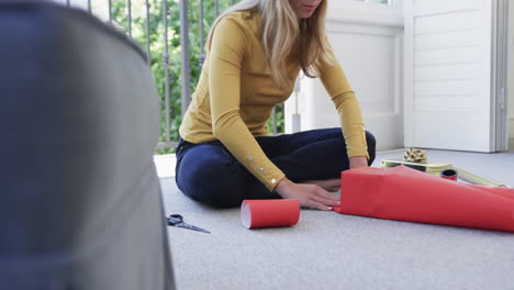 Biracial-woman-sitting-on-floor-packing-christmas-presents,-slow-motion