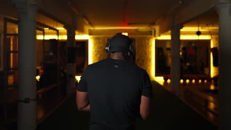 african muscular fit man in sportswear entering dark gym in slow motion rear view