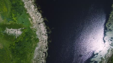 Drone-Flies-Down-Shore-of-a-Shimmering-Summertime-Grassy-Riparian-Blue-Water-Cattail-Island-Wetland-on-Outdoor-Lake-Habitat-Farmland-Park-in-Brandon-Manitoba-Canada