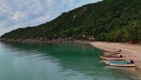 Aerial footage of a tropical beach with longtail boats and lush green hills in Thailand. Calm sea, soft sand, and vibrant landscape. Perfect for travel, tourism, relaxation, and adventure.