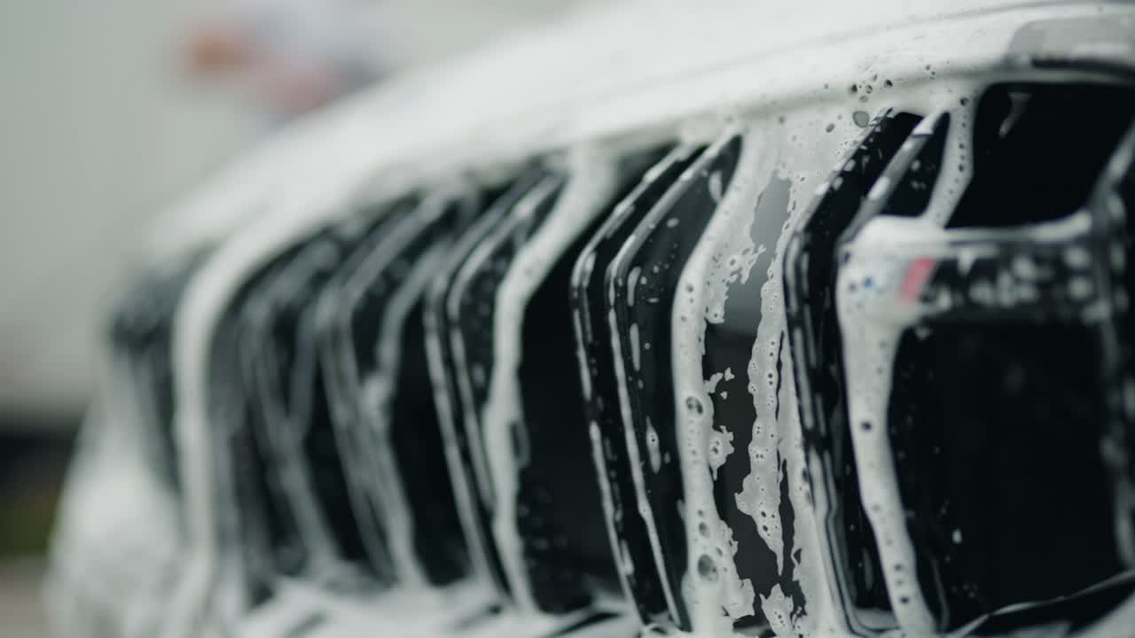 il sapone e l'acqua cadono tra la griglia del rene gemello di un'auto formando una piccola cascata interessante con riflessi