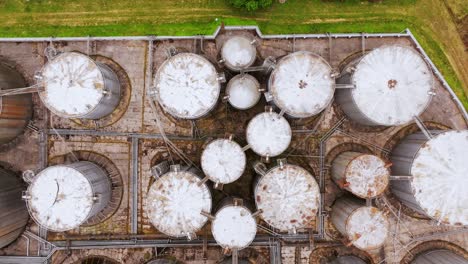 top-down flight reveals industrial pattern of storage tanks and weathered layout