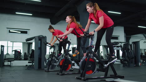 Group-of-girls-performs-aerobic-training-workout-cardio-routine-on-bike-simulators,-cycle-training