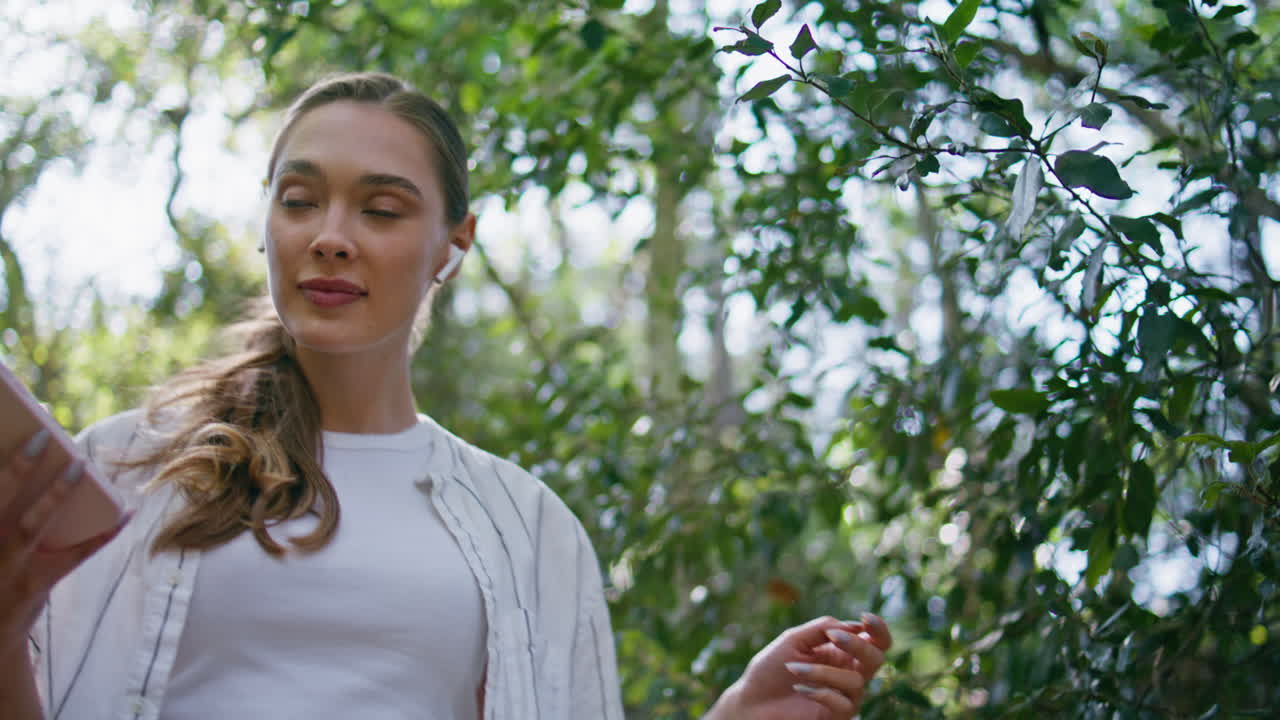 행복한 여성이 헤드폰으로 스마트폰을 걸어가는 클로즈업. 공원을 산책하는 예쁜 소녀