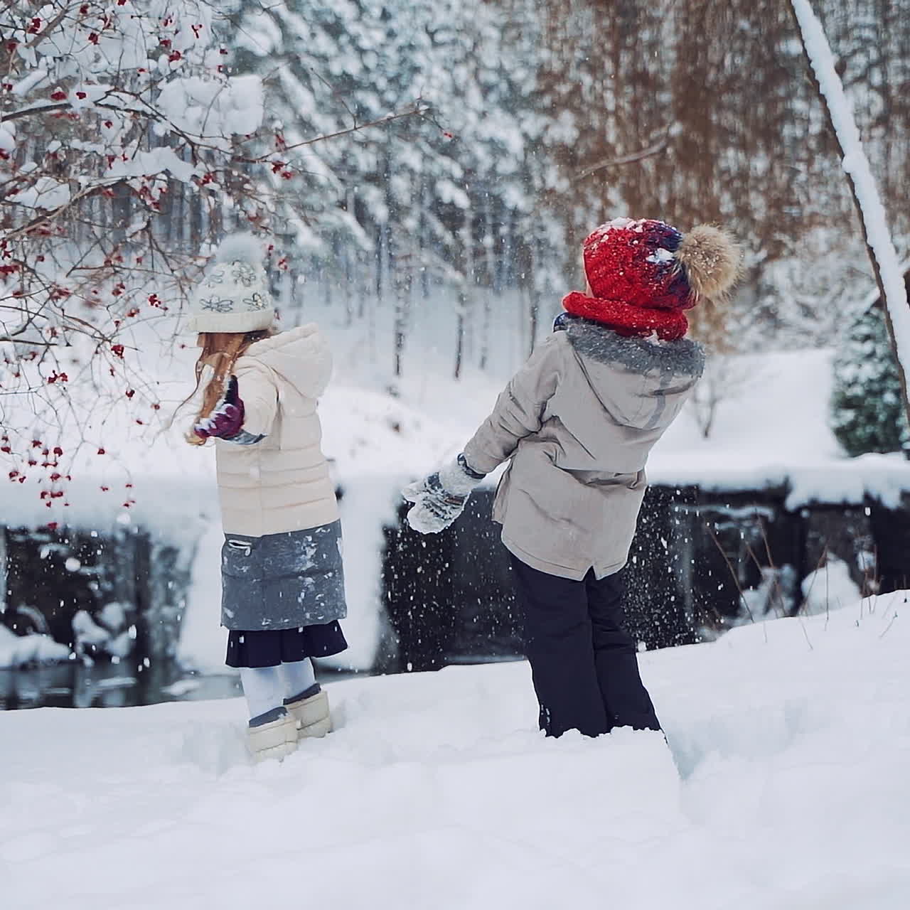 Happy children are playing with white snow together outdoors. Cheerful girls throw soft snow up over their heads in a beautiful forest in winter. Slow motion.