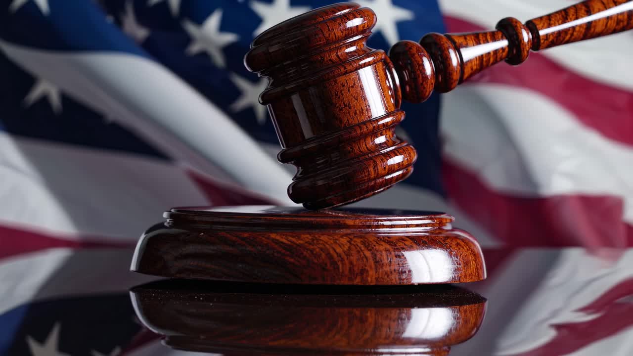 Wooden gavel on a reflective surface with a blurred American flag in the background