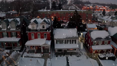 snow falls at traditional two story american homes covered in winter snowfall, decorated with christmas holiday lights