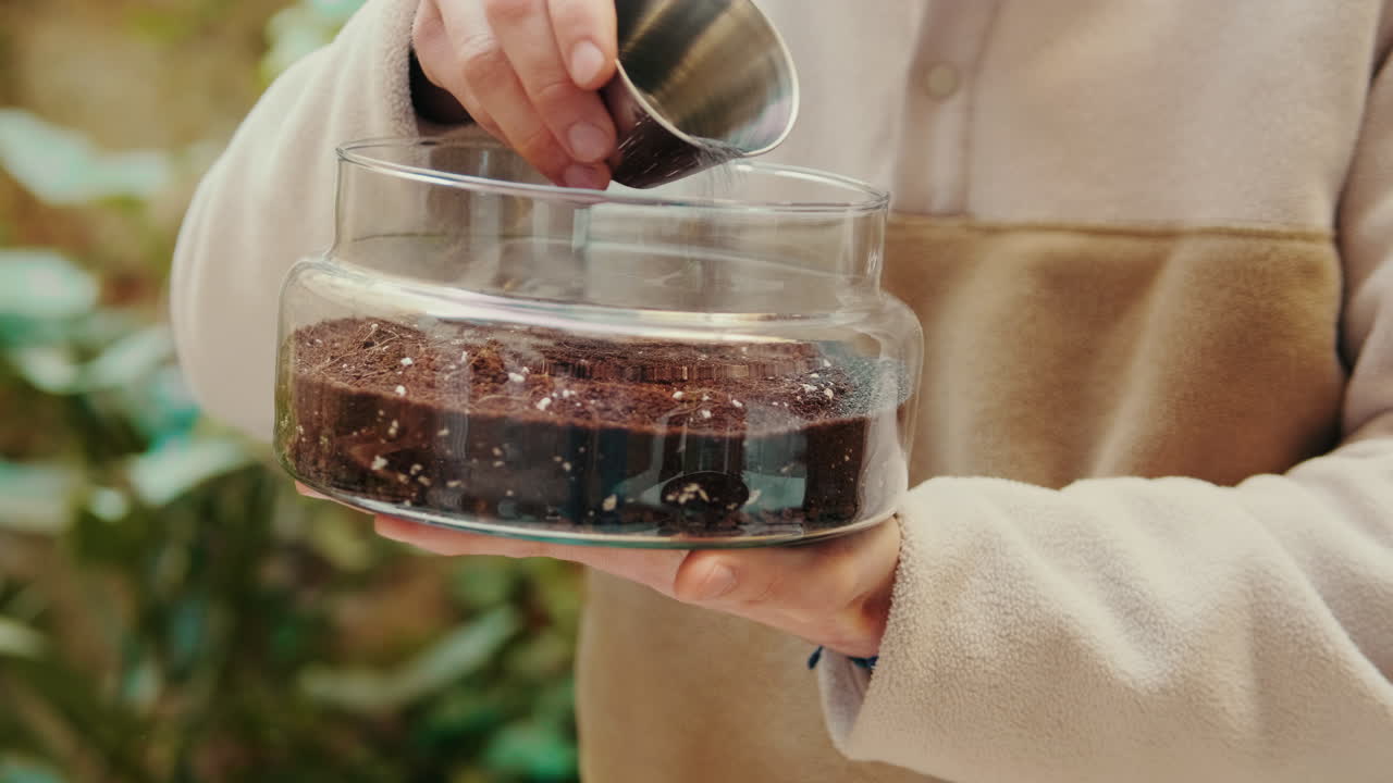 Hands Pouring Water into a Glass Jar with Soil