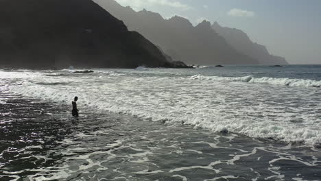 man walking against ocean waves,mountains behind,tenerife,canary islands,spain