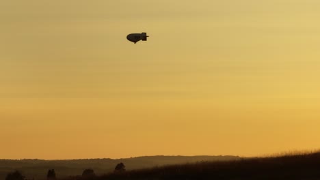 Silhouette-of-a-traveling-airship-in-the-sky-during-sunset-while-driving-on-land,-static-handheld