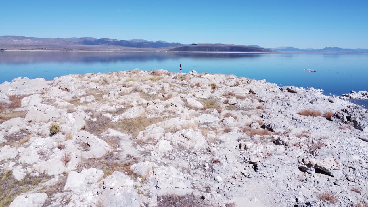 A man stands on a cliff edge as a drone pulls away from him.