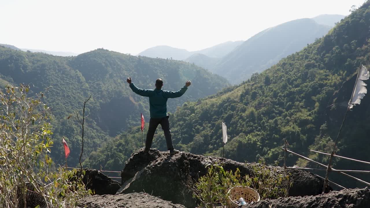 joven aislado en la cima de la montaña con bosques verdes y cielo azul brumoso por la mañana desde un video de ángulo plano tomado en mawryngkhang trek meghalaya india