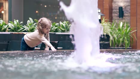 slow motion little sweet girl playing with water near fountain sprays water with a hand