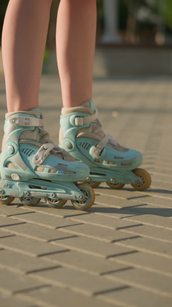 Leg view of person skating along interlocked path on rollerblades under warm sunlight casting shadows on ground, with blurred background featuring greenery and some structures