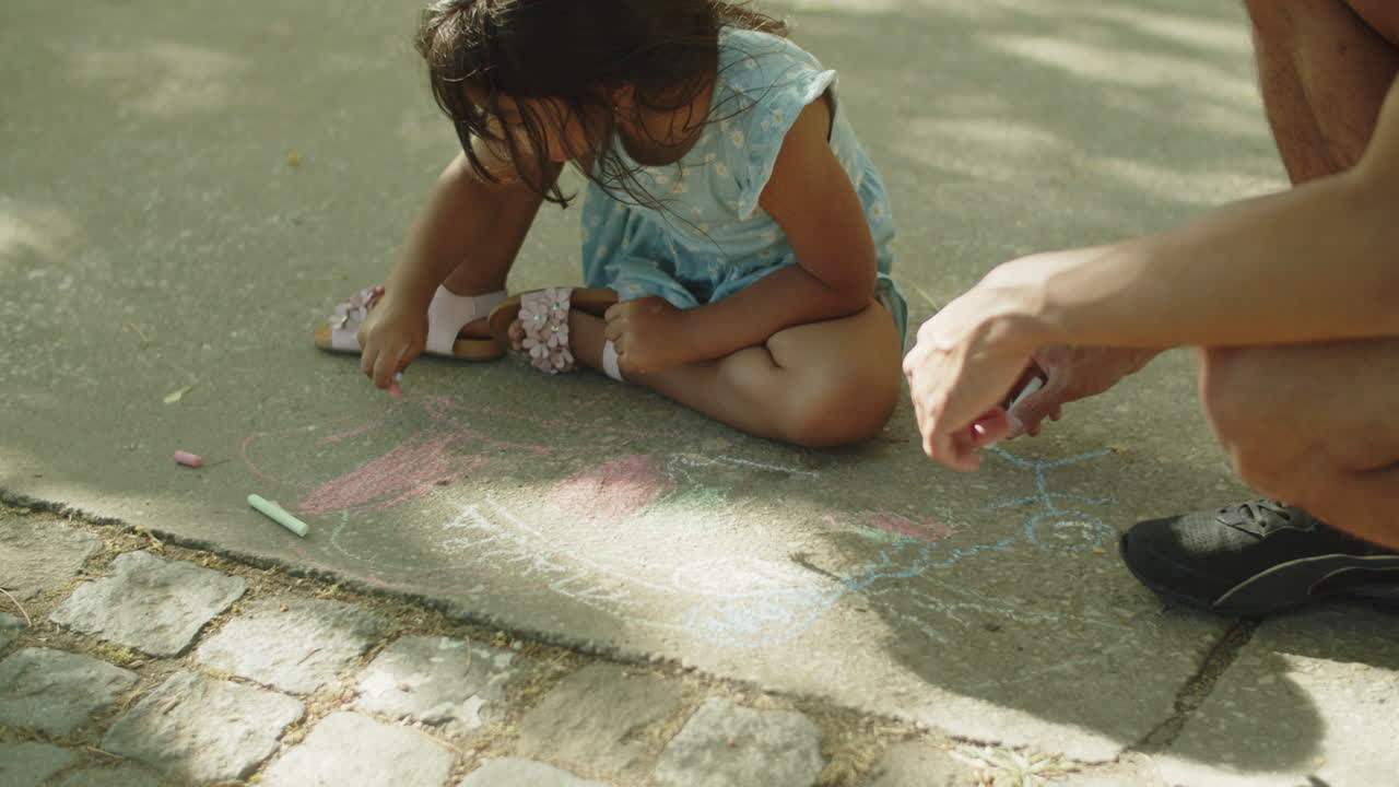 Father and child sitting on asphalt and drawing with chalks