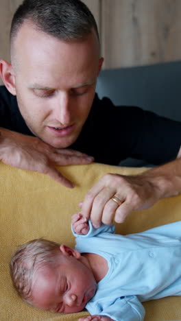 caucasian dad sitting over the crib with his newborn. father is talking to his son and touching him with tenderly. vertical video