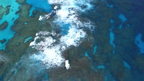 a drone shot of a blue lagoon reef with waves crashing during the day, displaying the crystal clear water, colorful coral reef, and the dynamic waves in a breathtaking aerial view