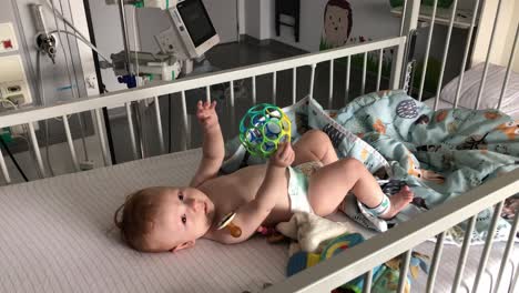 baby playing with a colourful ball in a hospital bed.