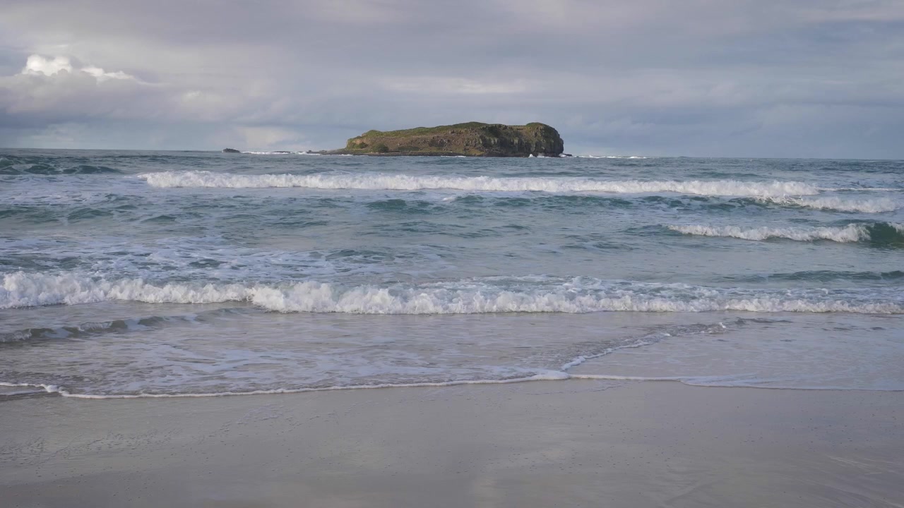 Handheld wide shot of Cook Island from Fingal Beach in afternoon light.