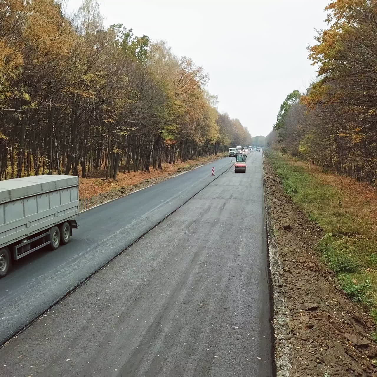 Cars moving on half of asphalt road in autumn. Road repair works on one side of the road at highway in the forest. Camera moves back.