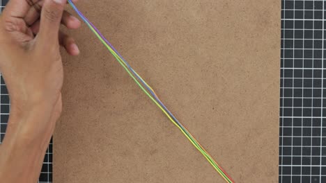 primo piano creando un braccialetto di macrame, mani abili tessono filati colorati dell'arcobaleno