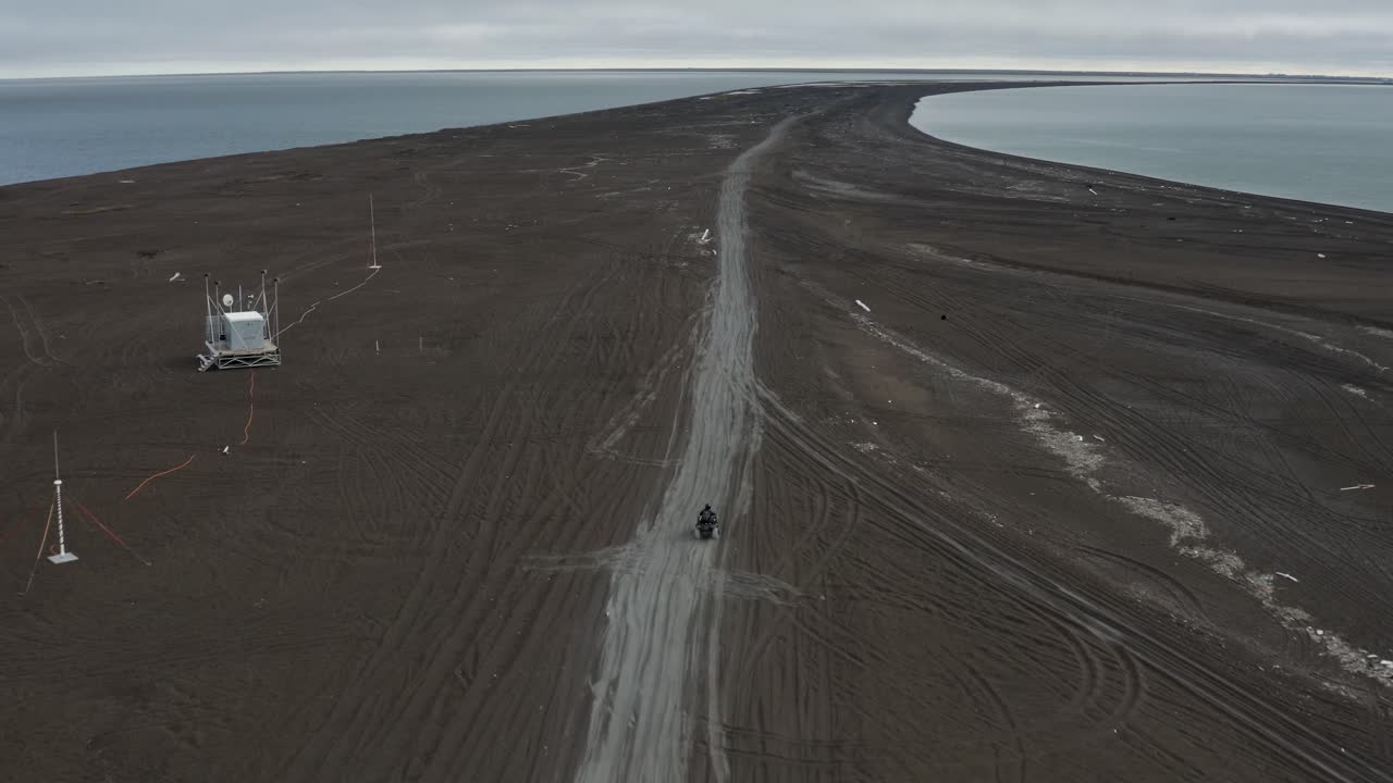 drone de seguimiento aéreo toma de un hombre solitario en un atv en la playa de arena negra en el punto más septentrional del ártico de los estados unidos cerca de barrow, alaska