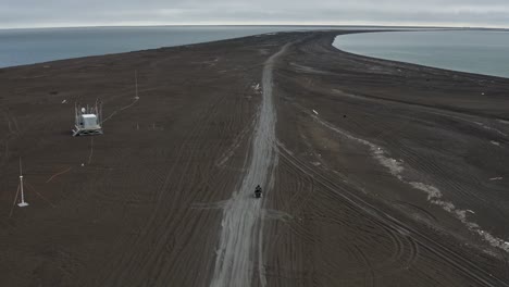 Luftverfolgungsdrohnenaufnahme-Eines-Einsamen-Mannes-Auf-Einem-Geländefahrzeug-Am-Schwarzen-Sandstrand-Am-Nördlichsten-Punkt-Der-Arktischen-Vereinigten-Staaten-In-Der-Nähe-Von-Barrow,-Alaska