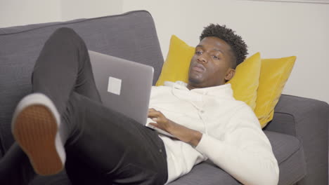 portrait of serious young student lying with laptop on couch