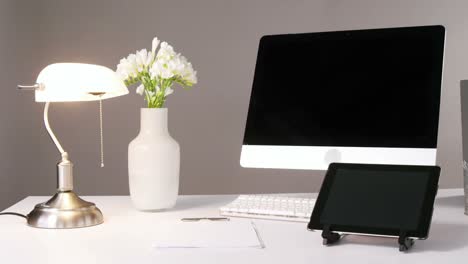 ordenador, tableta digital, lámpara de mesa y jarrón de flores
