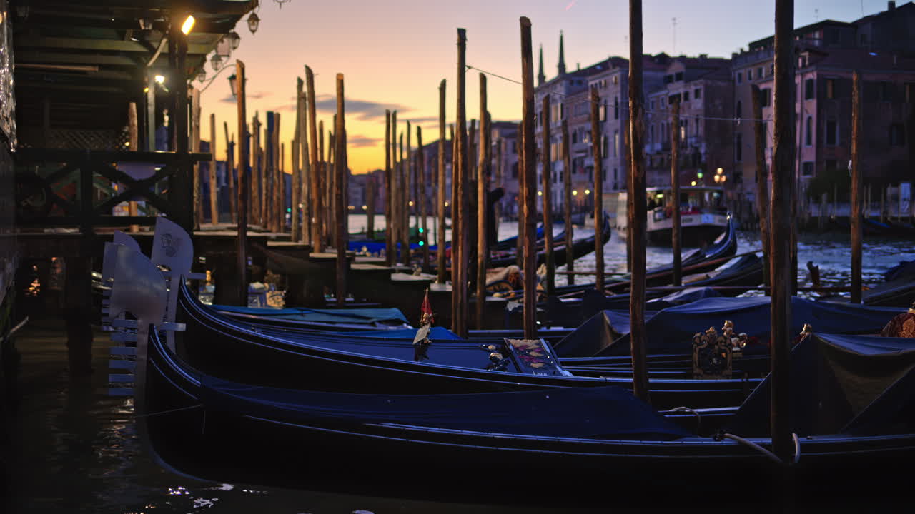 Multiple gondola boats docked on the side of the Grand Canal in Venice City, Italy at sunset