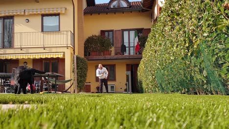 Mann-Wirft-Spielzeugball-In-Richtung-Kamera-Und-Schwarzer-Labrador-Springt-Und-Versucht,-Ihn-Zu-Fangen