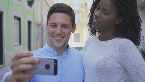 vista frontal de una joven pareja alegre tomando una selfie con un teléfono inteligente.