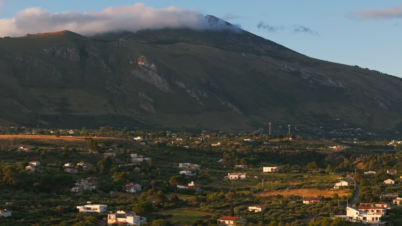 Aerial drone descending over clouds on mountain peak, revealing empty Guidaloca Beach in Sicily, Italy, with tranquil waves and serene golden sunrise light