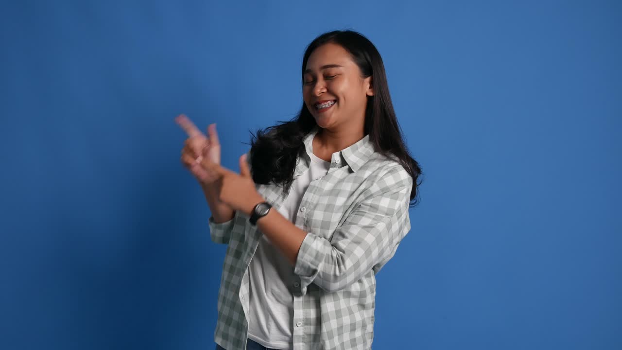 Shocked smiling young asian woman posing isolated on blue background studio. People lifestyle concept. Looking camera pointing index finger aside say wow