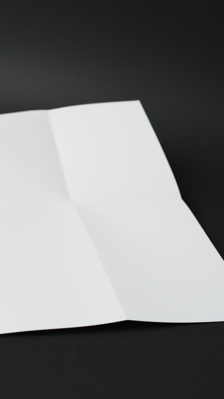 Vertical video of piece of white paper with creases on black background
