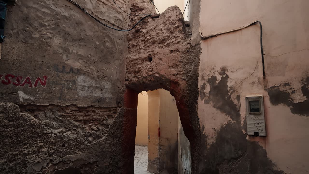 Muro di pietra usurato con angolo ad arco che conduce in un passaggio nella Medina di Marrakech