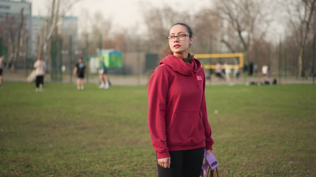 Woman Observing Game Attentively, Female Trainer With Gear Quietly Preparing To Instruct Athletes, Young Woman In Red Hoodie Observing Sports Activity With Focused Attention And Readiness