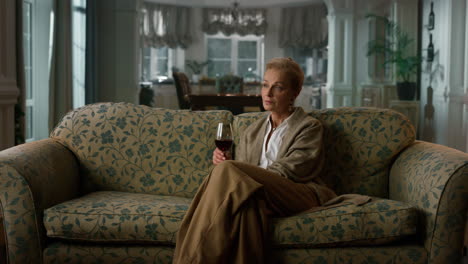 rich senior woman drinking red wine in luxury apartment