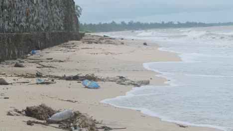 waves washing up on a sand beach covered in plastic trash garbage rubbish debris slow motion wide